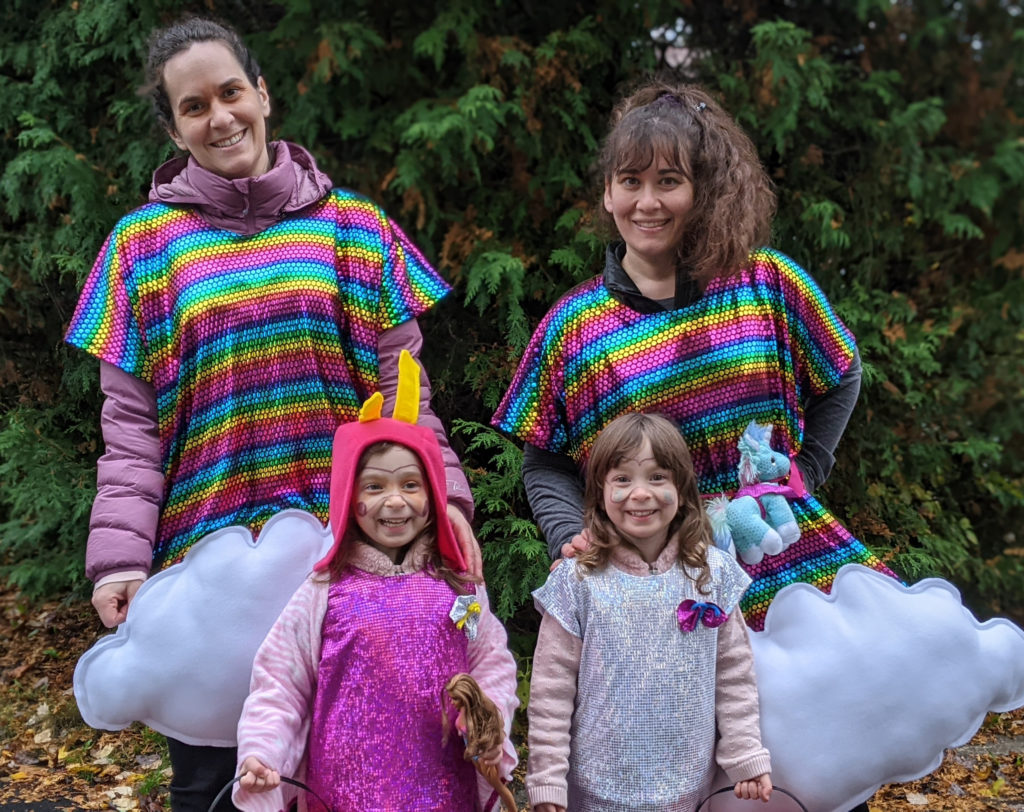 Two Savvy Girls dressed as rainbows standing with two excited toddlers dressed for Halloween.
